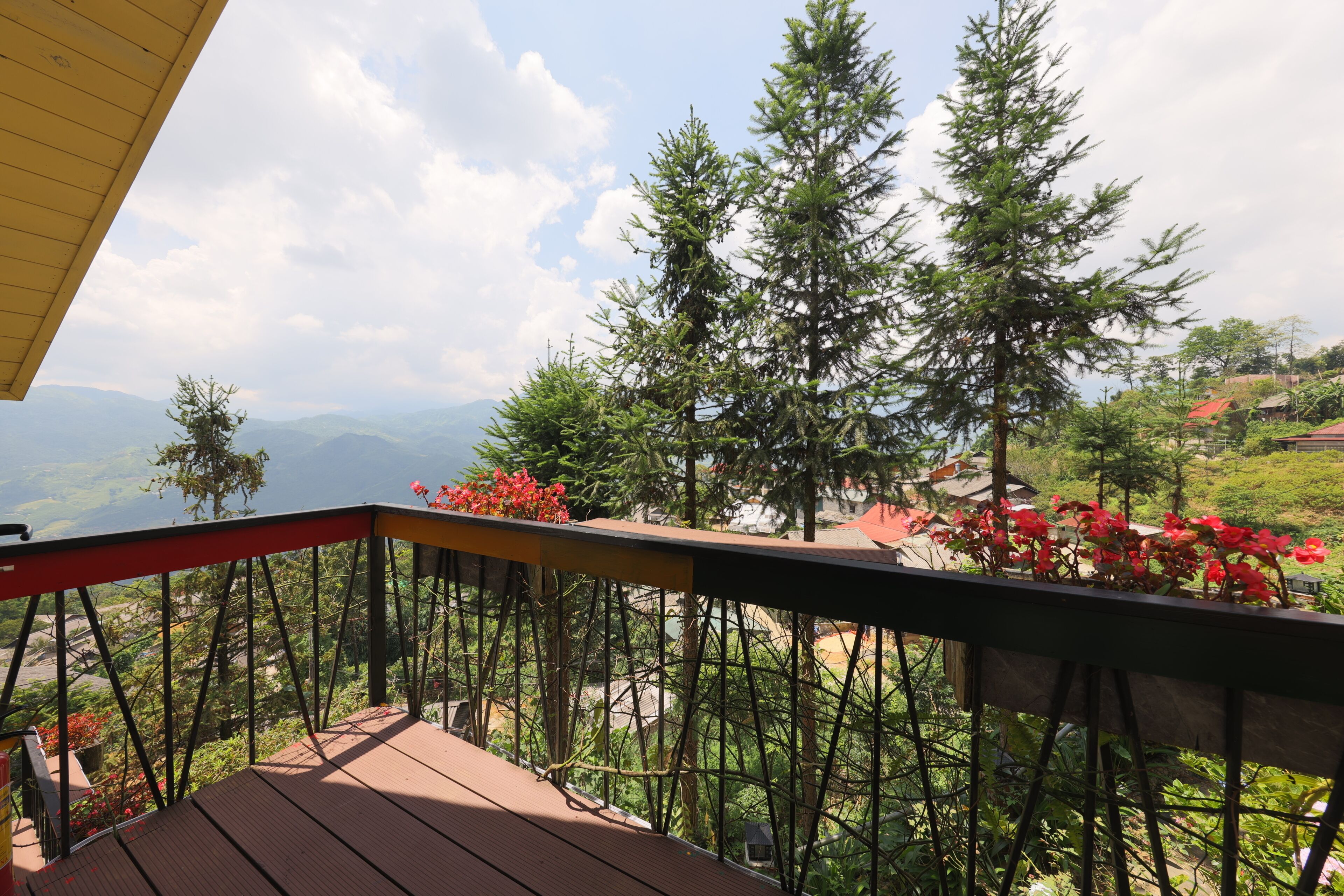 A wooden deck with a metal railing overlooking a mountainous landscape with trees and houses.