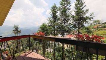 A wooden deck with a metal railing overlooking a mountainous landscape with trees and houses.