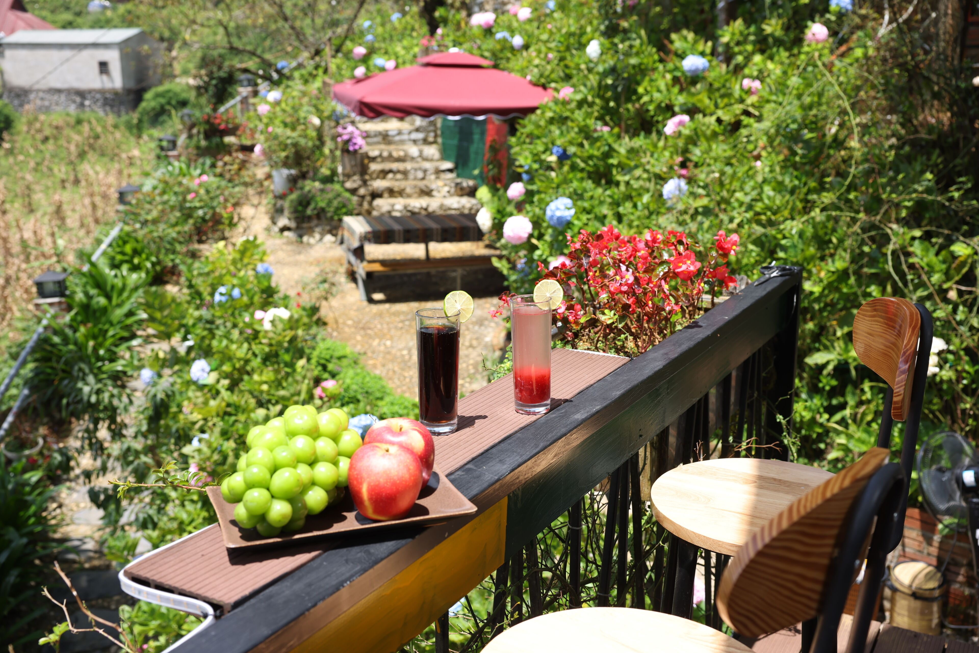 Un jardín con una mesa que tiene una bandeja de fruta, una bebida y una silla.