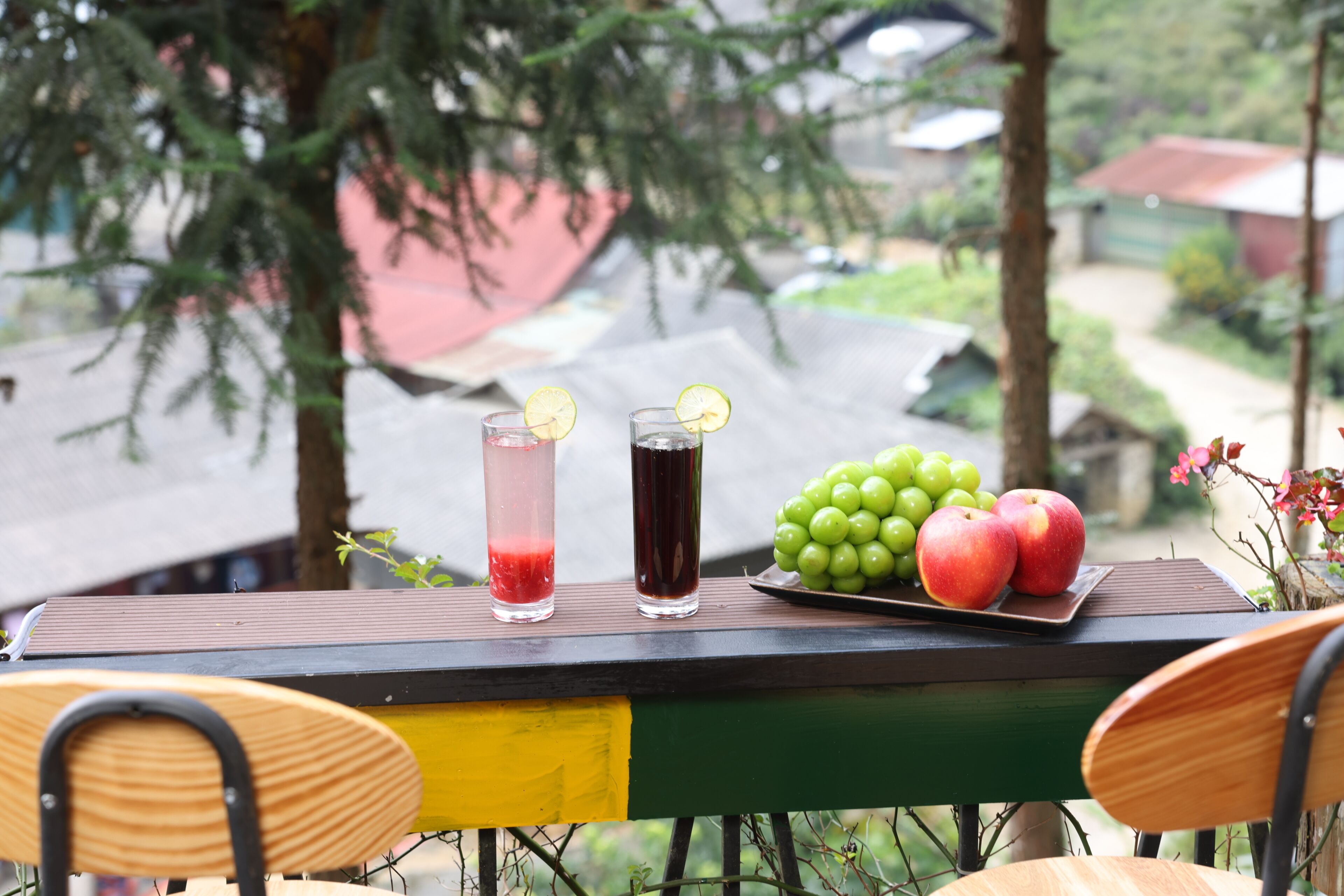 Une table avec deux verres contenant des boissons, une assiette de raisins et deux pommes.