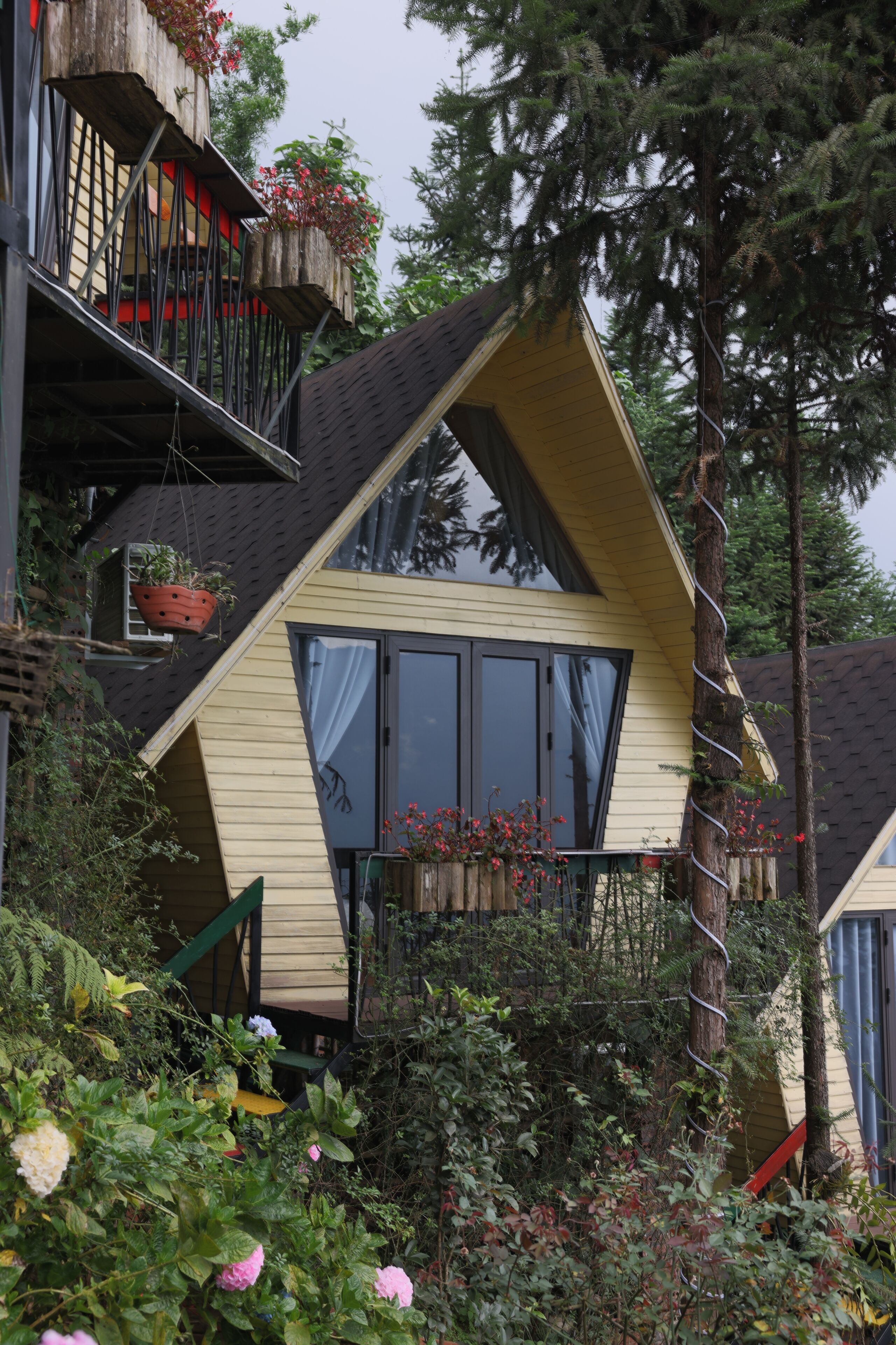 Een huis met een schuin dak, grote ramen en een balkon met bloempotten.