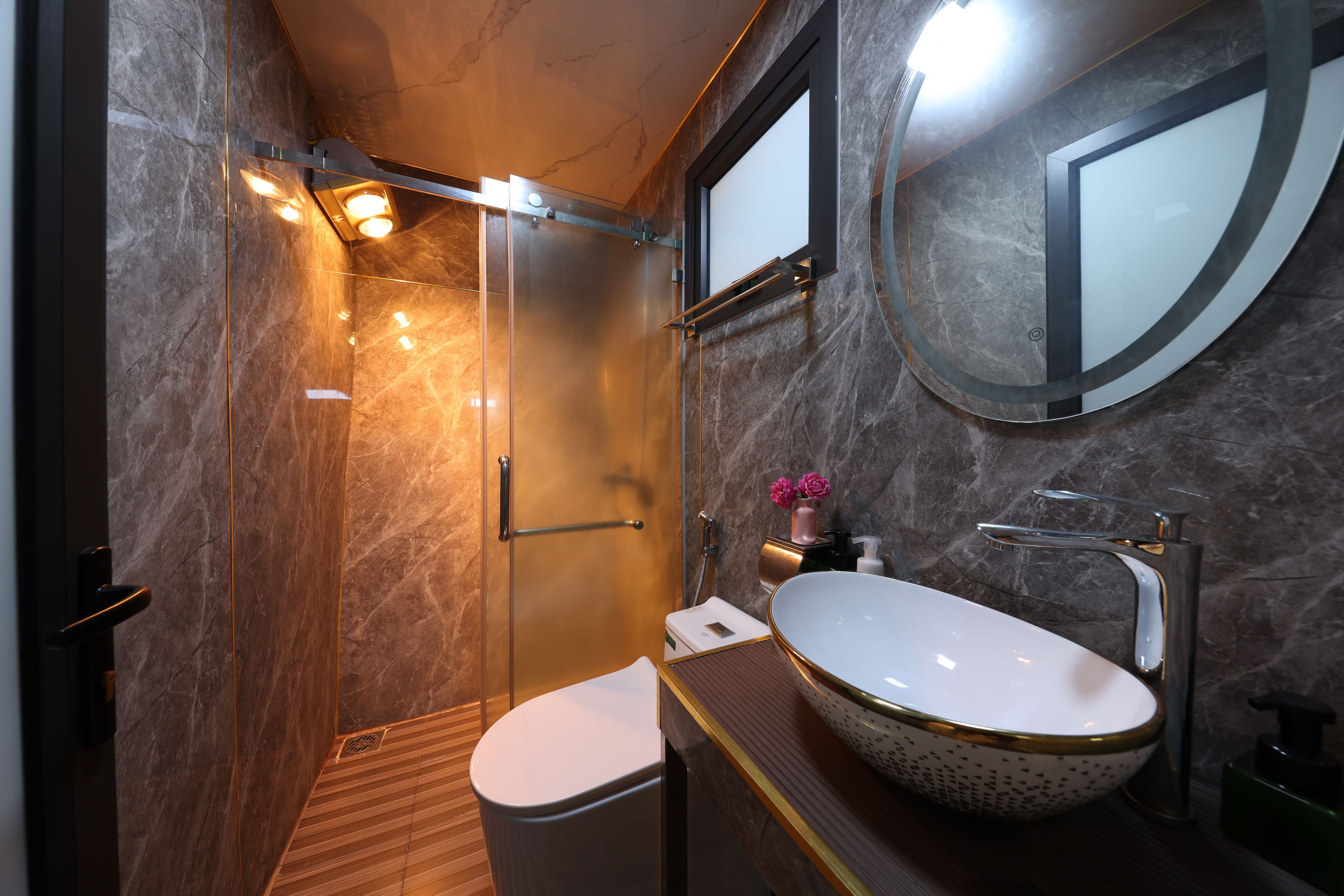 Een moderne badkamer met een groot ovaal wastafel, toilet en een douche met glazen wanden.