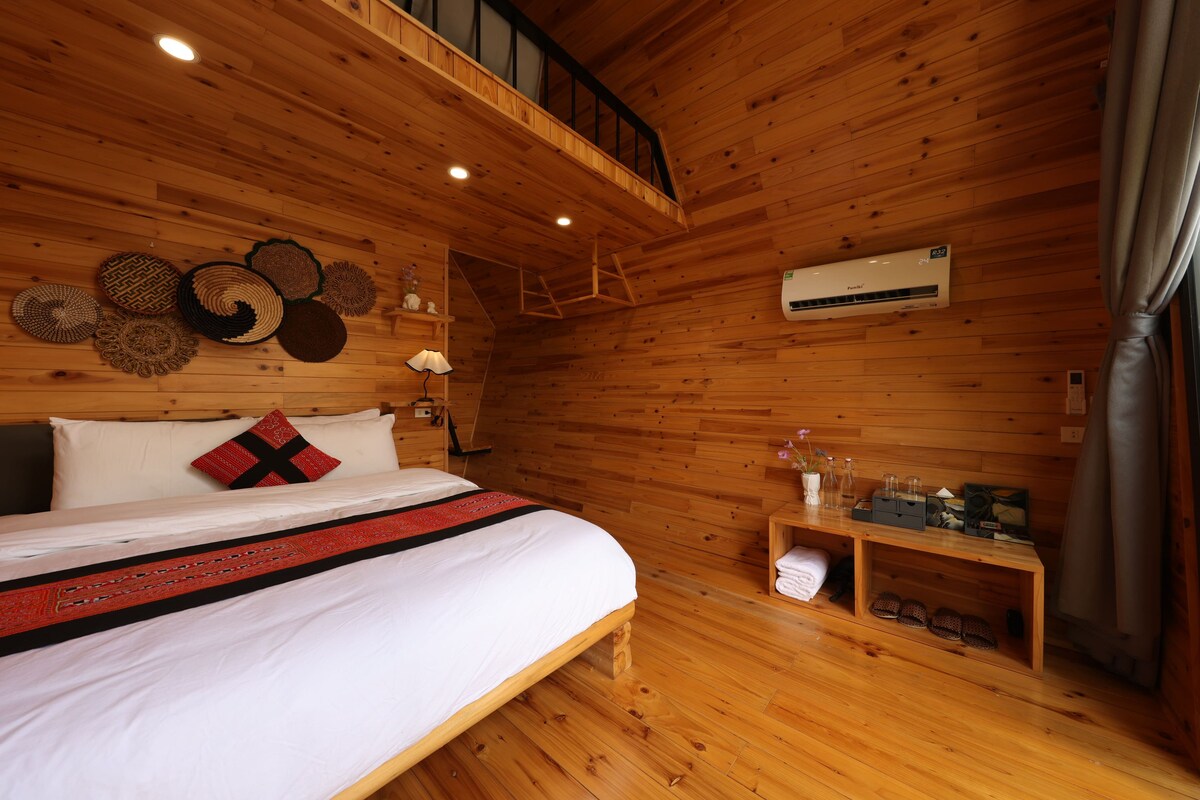 A wooden cabin bedroom with a bed, pillows, a nightstand, and a ceiling fan.