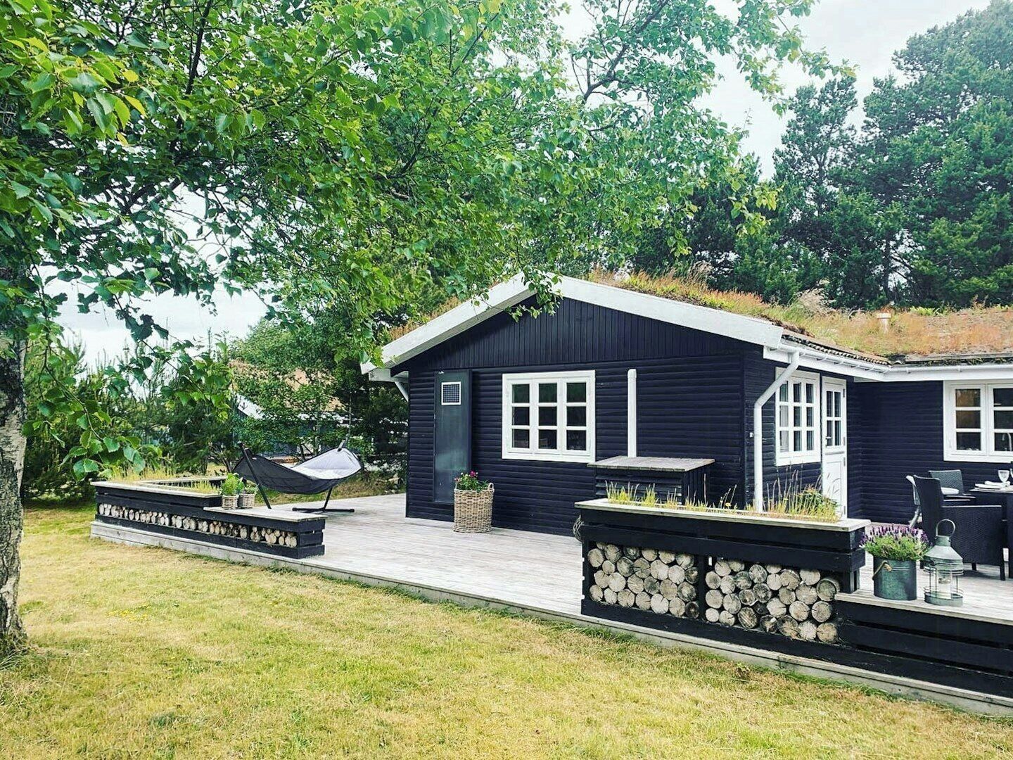 Eine schwarze Holzhütte mit Veranda, einem Hängesessel und einer Feuerstelle.