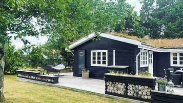 Eine schwarze Holzhütte mit Veranda, einem Hängesessel und einer Feuerstelle.