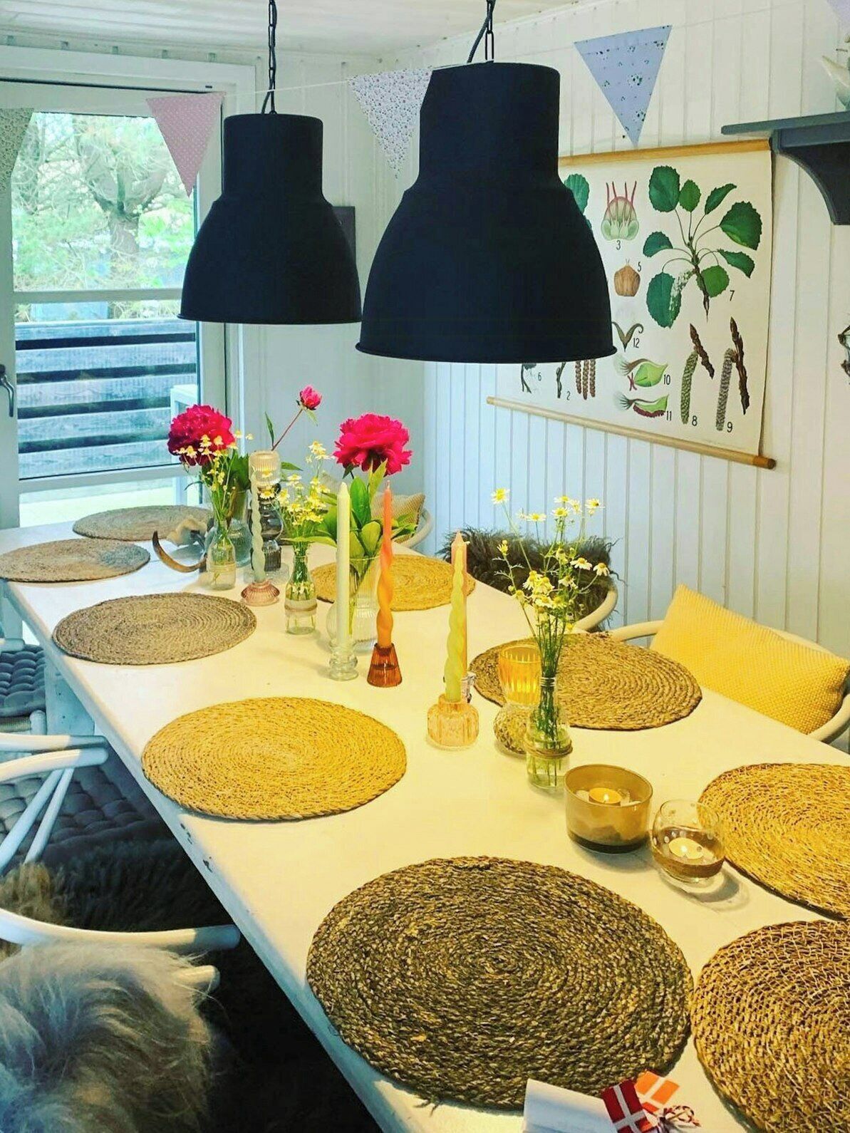 Ein Esstisch, gedeckt mit gewebten Tischsets, Kerzen und Blumenarrangements.
