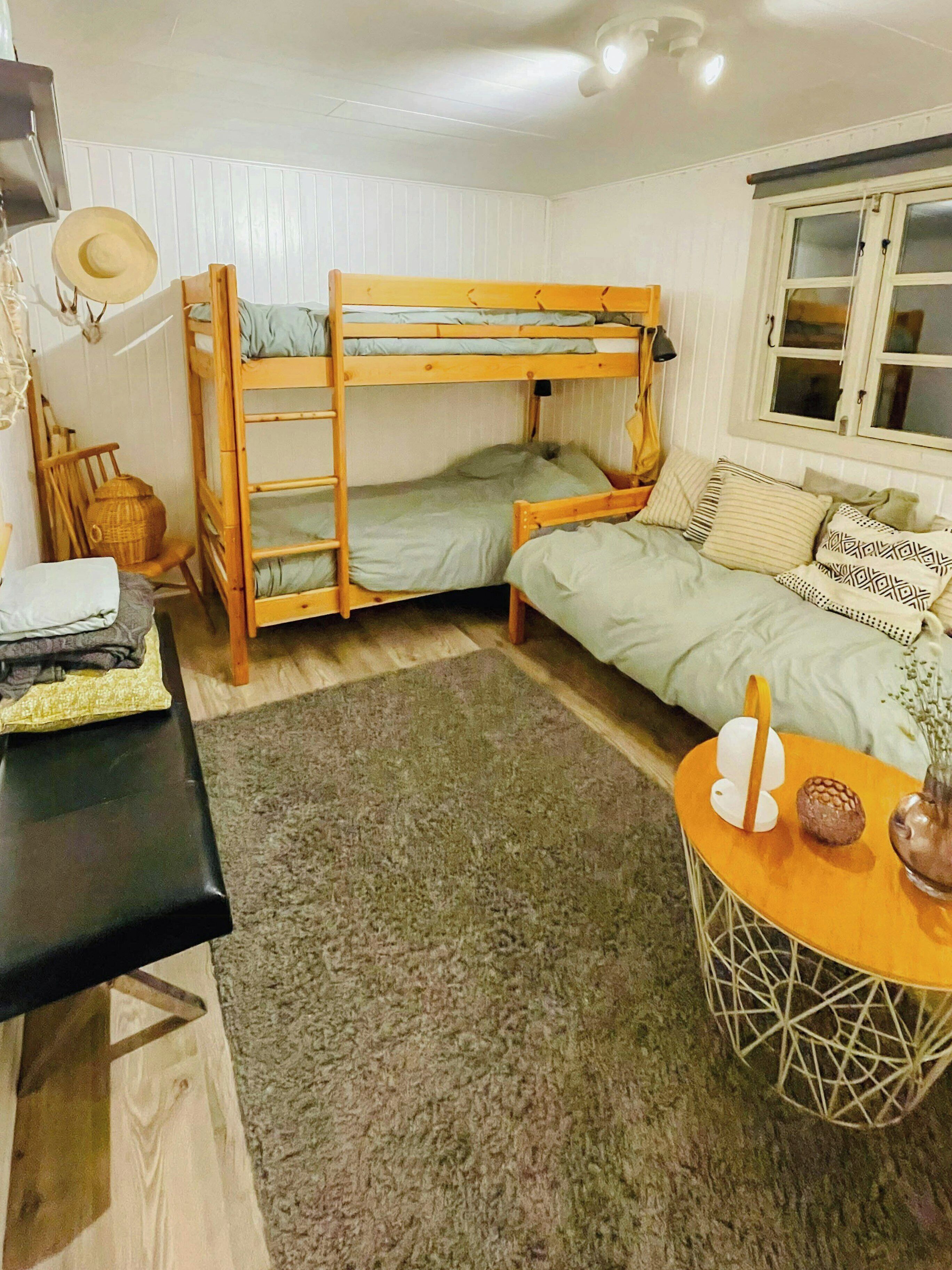 A bunk bed with a ladder, a sofa with patterned cushions, a small round table with a vase, and a lamp on a desk.