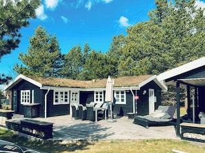 Eine Hütte mit einer Terrasse, Sitzgelegenheiten im Freien und einem überdachten Bereich.