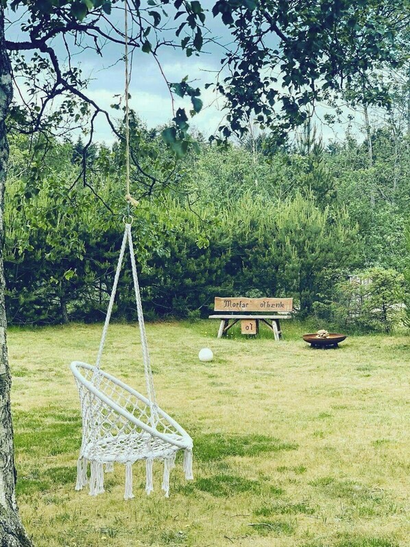 A hammock suspended from a tree in a grassy area with a wooden sign and a bowl in the background.