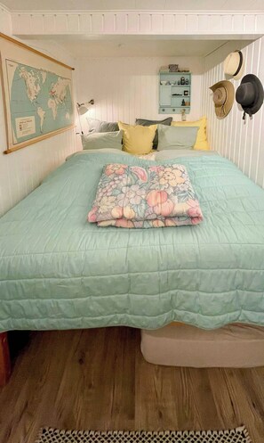 A bedroom with a bed, pillows, a world map, and a hat on the wall.