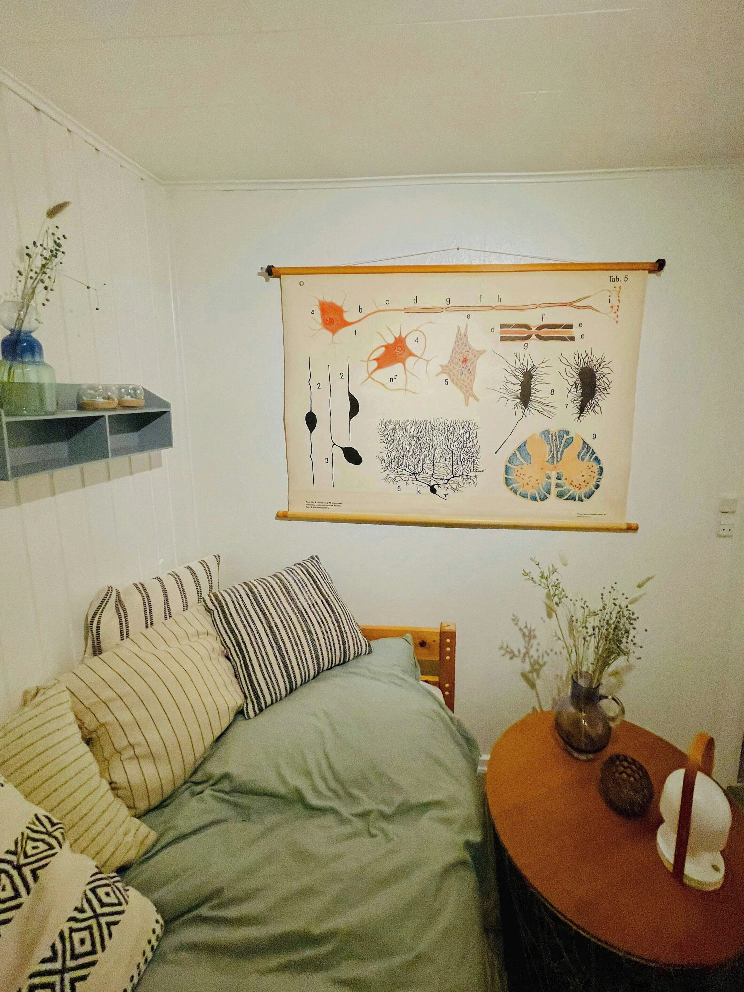 Ein Schlafzimmer mit einem Bett, Kissen, einem Nachttisch mit einer Vase und einer Wanddekoration.
