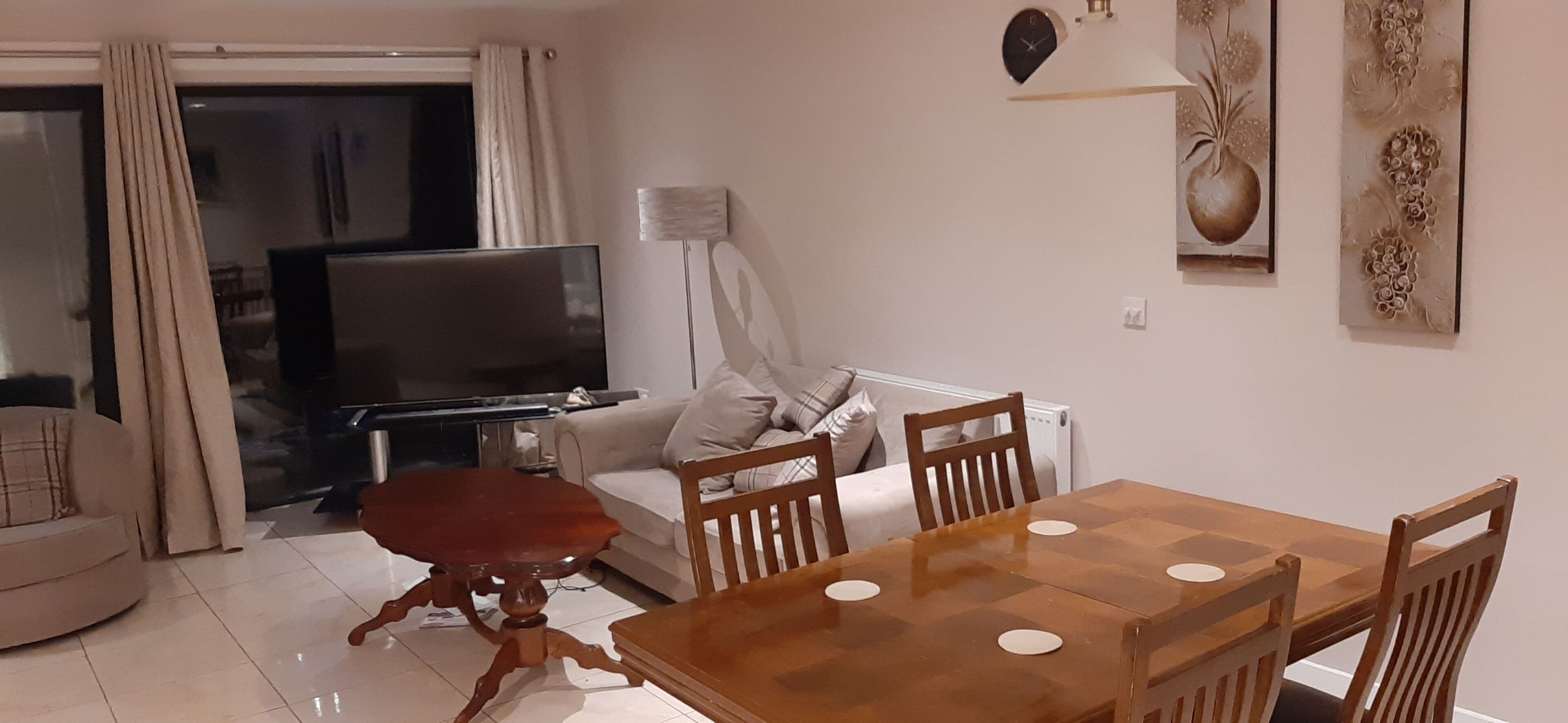 Ein Wohnzimmer mit Fernseher, Sofa und Esstisch.