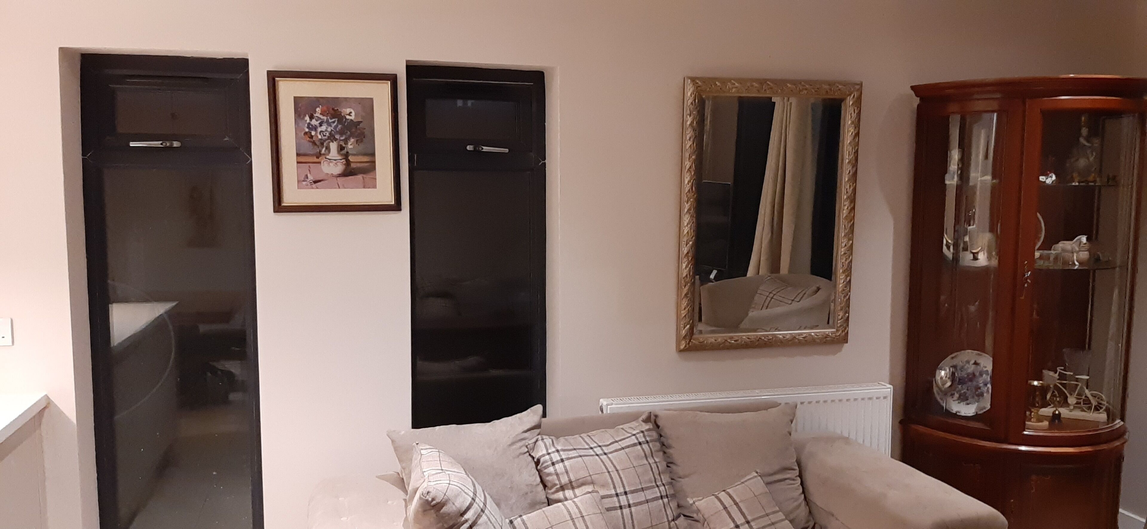 A living room with a sofa, a cabinet with glass doors, and two framed pictures on the wall.