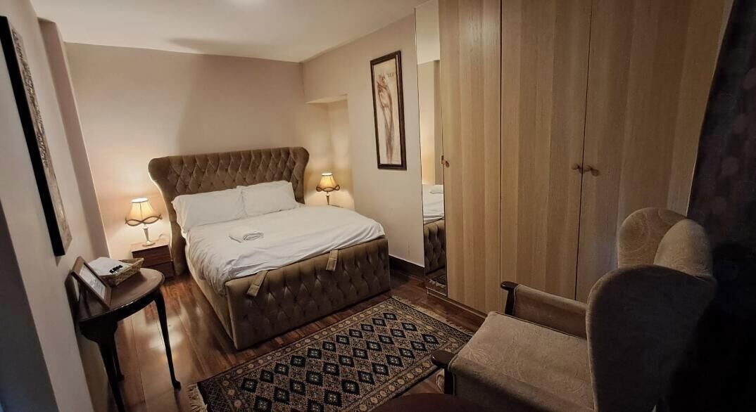 A hotel room with a large bed, bedside lamps, a wooden wardrobe, and a patterned rug.