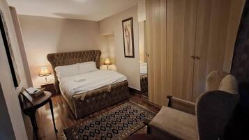 A hotel room with a large bed, bedside lamps, a wooden wardrobe, and a patterned rug.