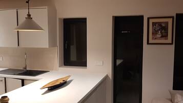 Una cucina moderna con un piano di lavoro bianco, una lampada a sospensione, una finestra con cornice nera e un quadro appeso al muro.
