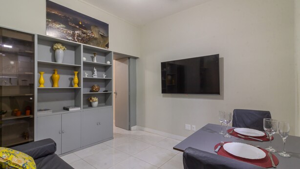 Una sala moderna con comedor, armarios grises, un televisor de pantalla plana y un sofá con cojines estampados.