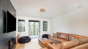A modern living room with a leather sofa, a flat-screen TV, and a fireplace. - Luxe Telluride Oasis - Hot Tub & Deck & Views (Mountain Village)