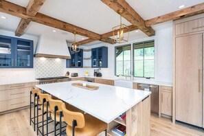 A modern kitchen with a large island, wooden beams, and bar stools. - Luxe Telluride Oasis - Hot Tub & Deck & Views (Mountain Village)