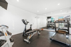 Ein Fitnessstudio mit Trainingsgeräten, darunter Laufband, Ergometer und Gewichte.