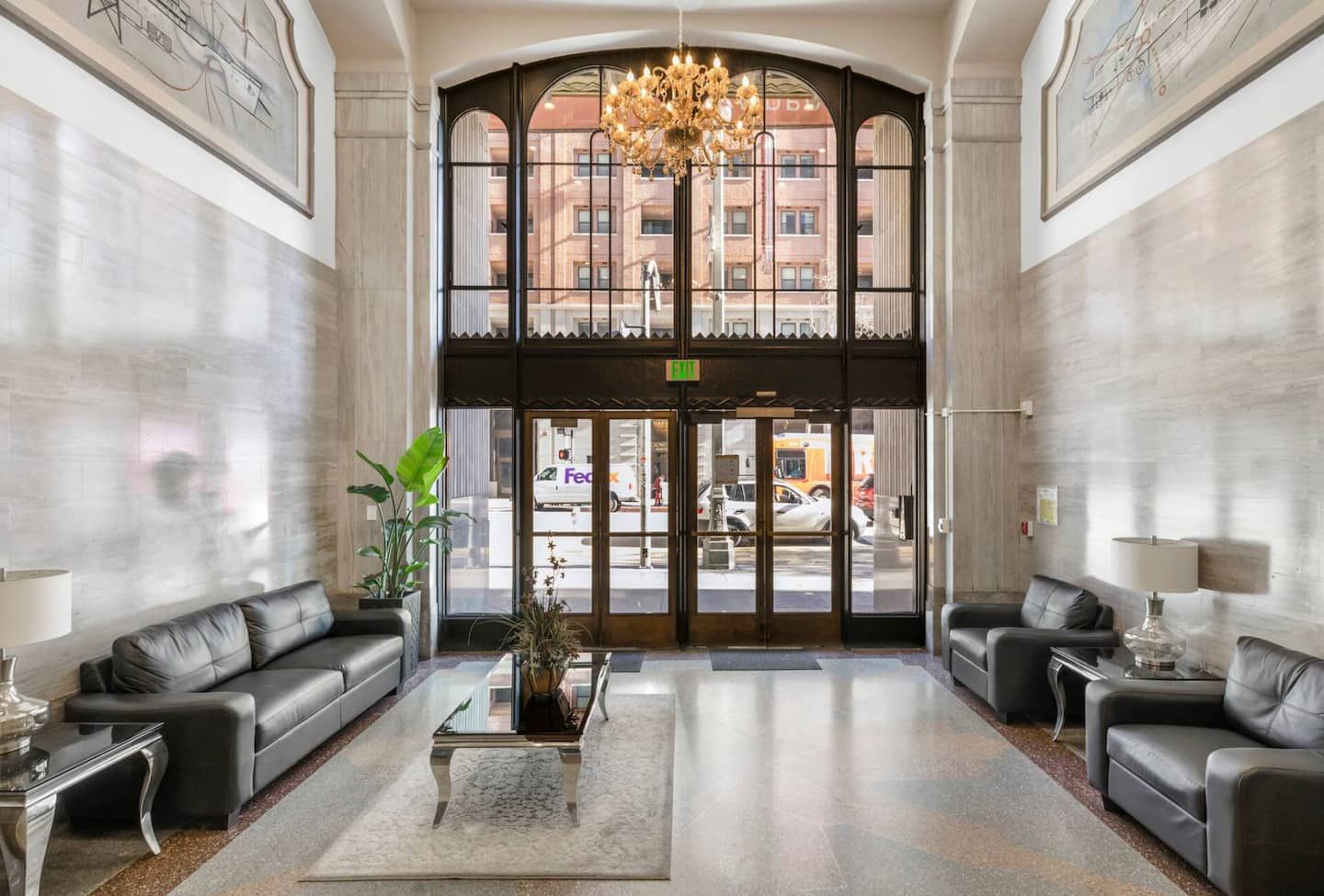 A lobby with a grand chandelier, leather sofas, and a view of the street through large glass doors.