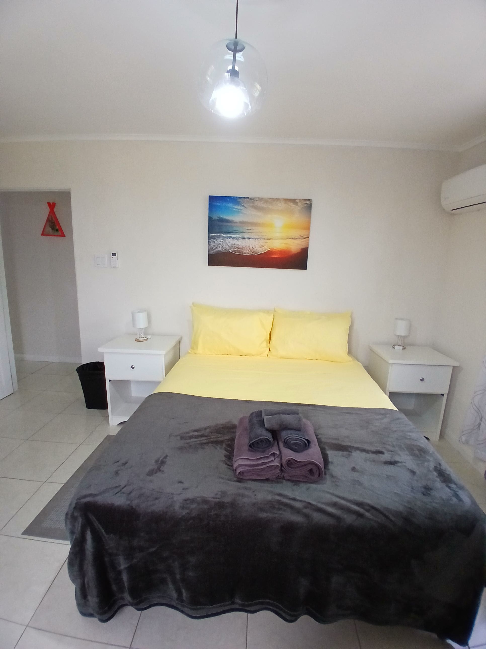 Een slaapkamer met een bed, twee nachtkastjes, een kunstwerk aan de muur en een hanglamp.