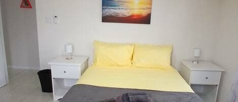 Quarto com cama, duas mesas de cabeceira, uma obra de arte na parede e um lustre.