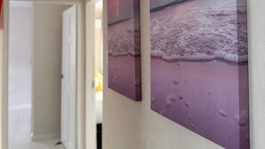 Ein Flur mit einer Tür zu einem anderen Raum, einem Lichtschalter und einem Wandbild, das eine Strandansicht zeigt.