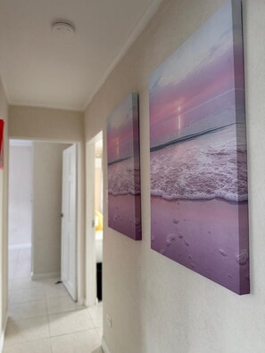 Ein Flur mit einer Tür zu einem anderen Raum, einem Lichtschalter und einem Wandbild, das eine Strandansicht zeigt.