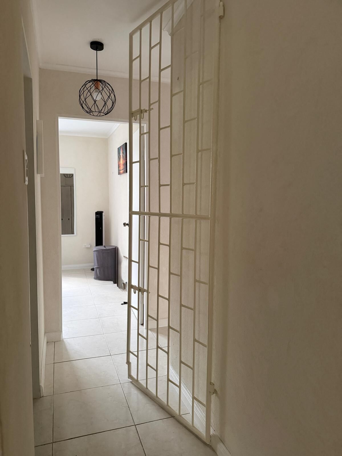 Un couloir avec une porte blanche, un luminaire au plafond et un sol carrelé.