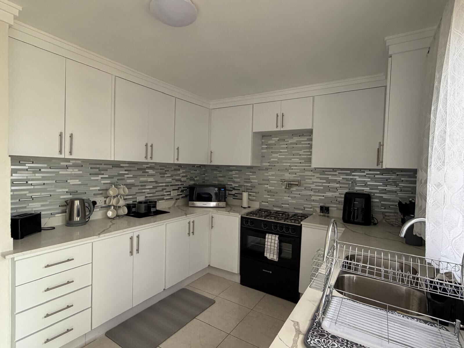 A modern kitchen with white cabinets, a black stove, a microwave, and a tiled backsplash.