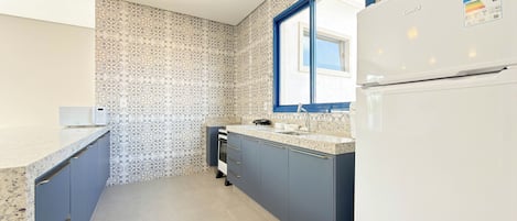 A compact kitchen with a microwave, sink, and stove, featuring patterned wallpaper and a window.