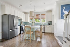 A modern kitchen with white cabinetry, stainless steel appliances, and a central island with chairs. - Sully & Sonshine | 3 BR Near Sullivan's Island (Mount Pleasant)