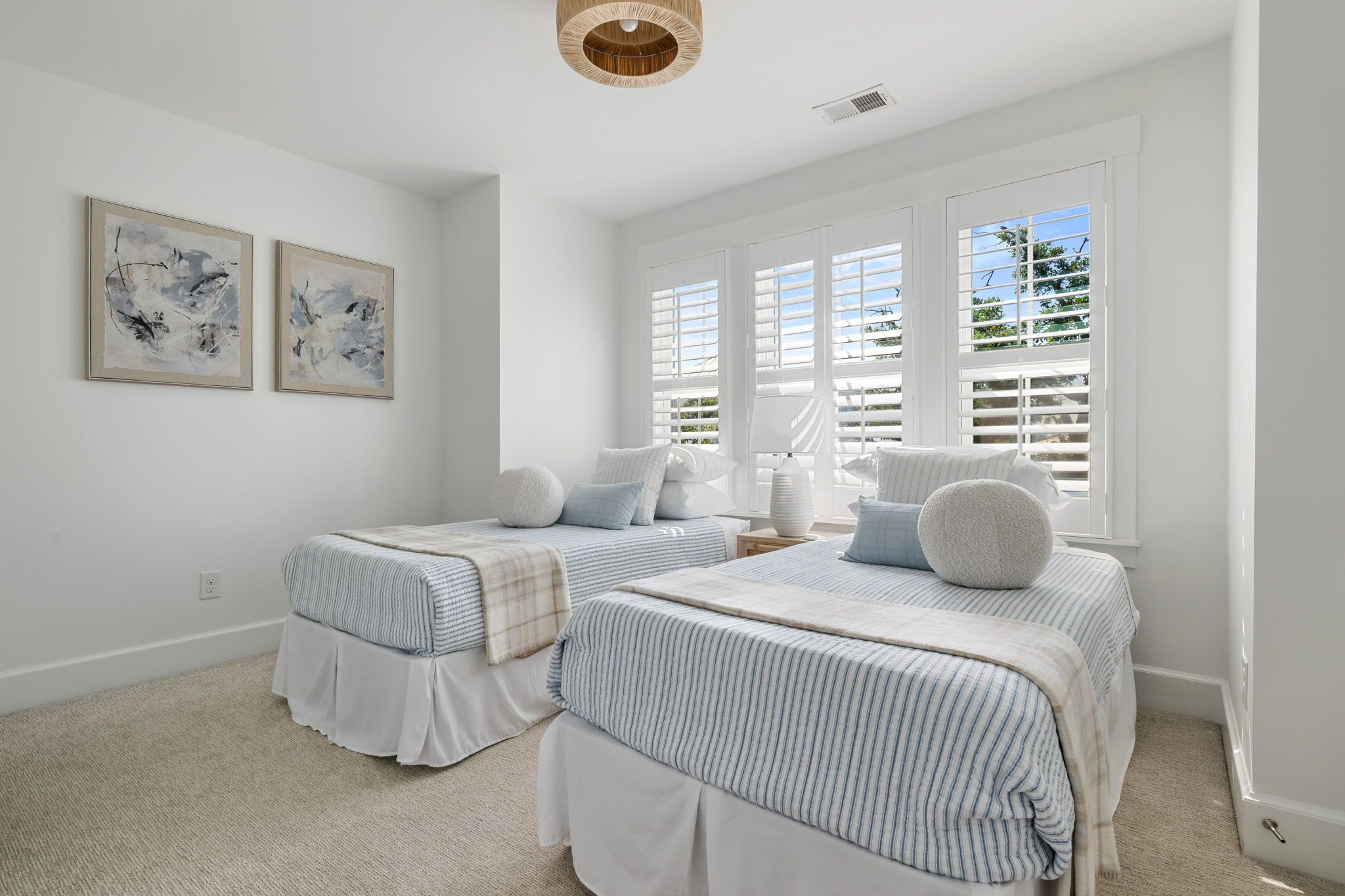 A bedroom with two beds, a large window with shutters, and two abstract paintings on the wall.