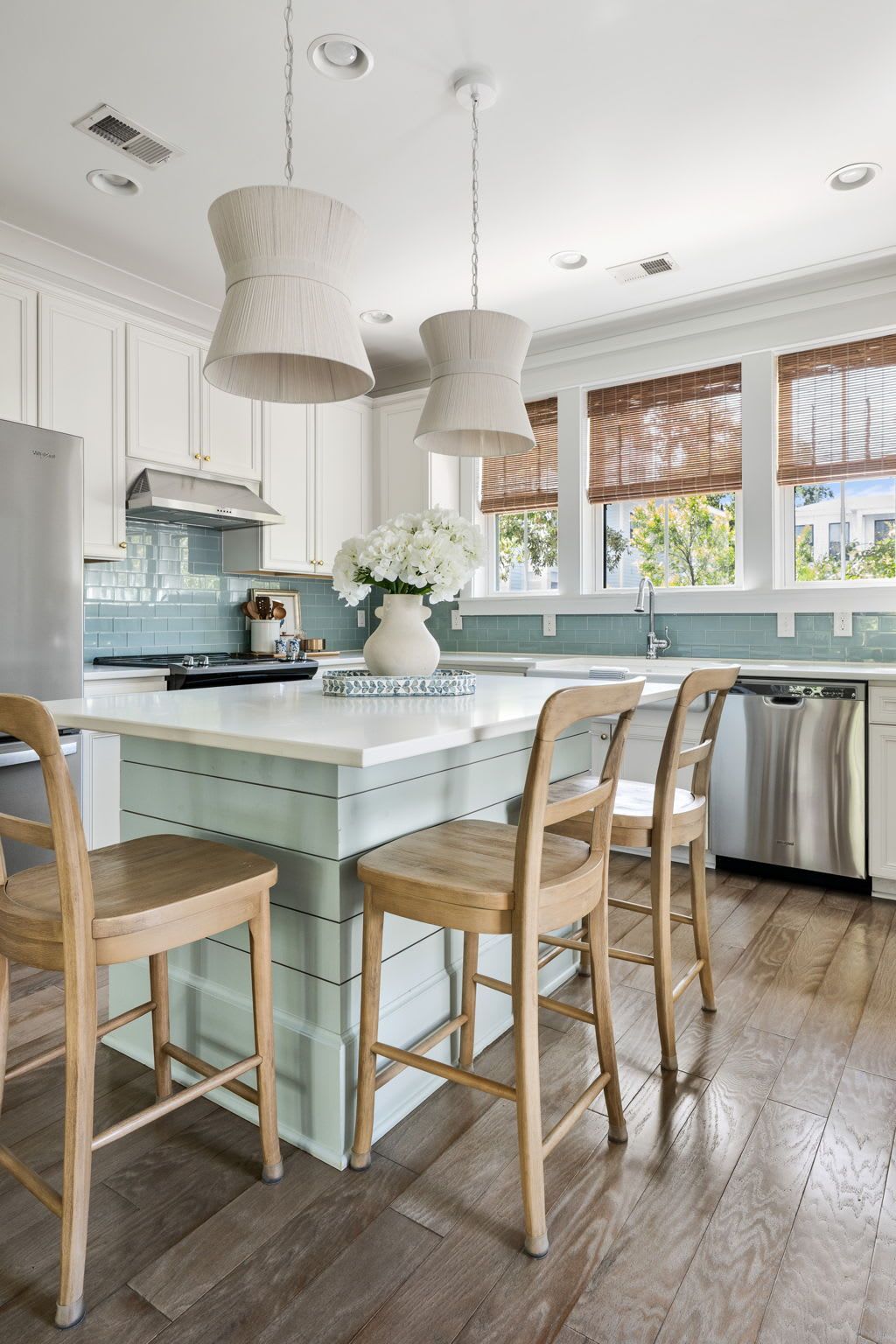 A modern kitchen with white cabinetry, a central island with bar stools, pendant lighting, and a dishwasher.