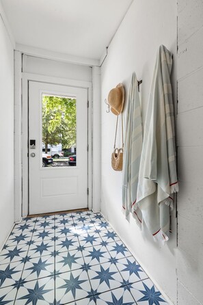 Ein Flur mit einer weißen Tür, einem gemusterten Boden und einer Wand mit Handtüchern und einem Hut.