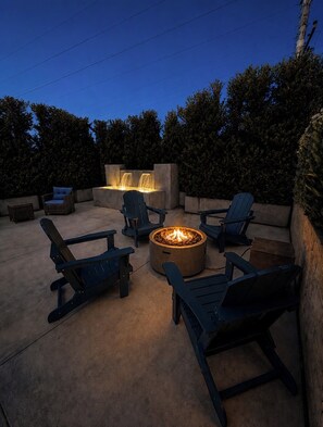 An outdoor seating area with Adirondack chairs, a fire pit, and a built-in water feature.