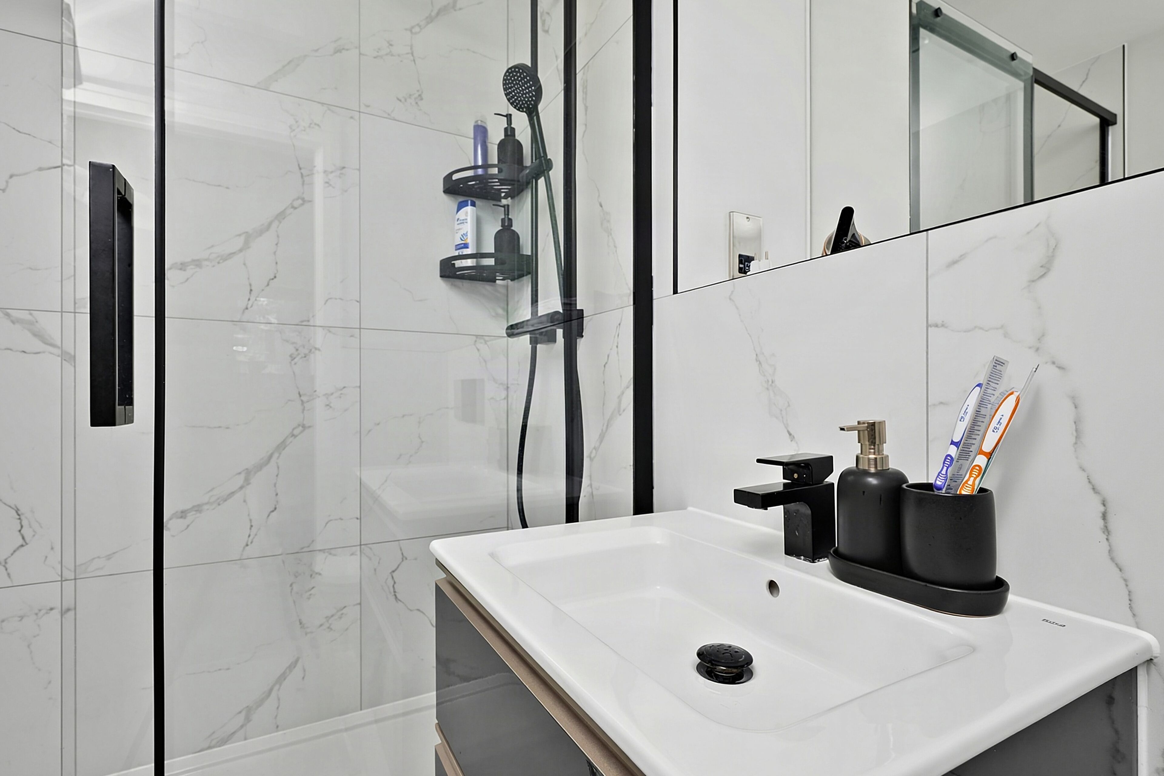 Un baño moderno con un lavamanos blanco, dispensador de jabón negro y un porta cepillos de dientes con cepillos.