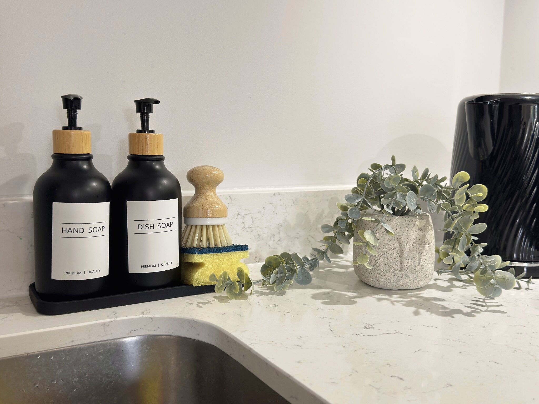 A kitchen counter with two bottles of soap, a brush, and a potted plant.