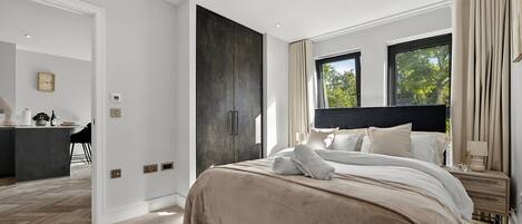 A modern bedroom with a large bed, a dark accent wall, and a view of trees through the window.