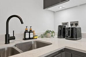 Una cocina con un grifo moderno, un lavamanos y una encimera con dos tostadoras y una pequeña planta.