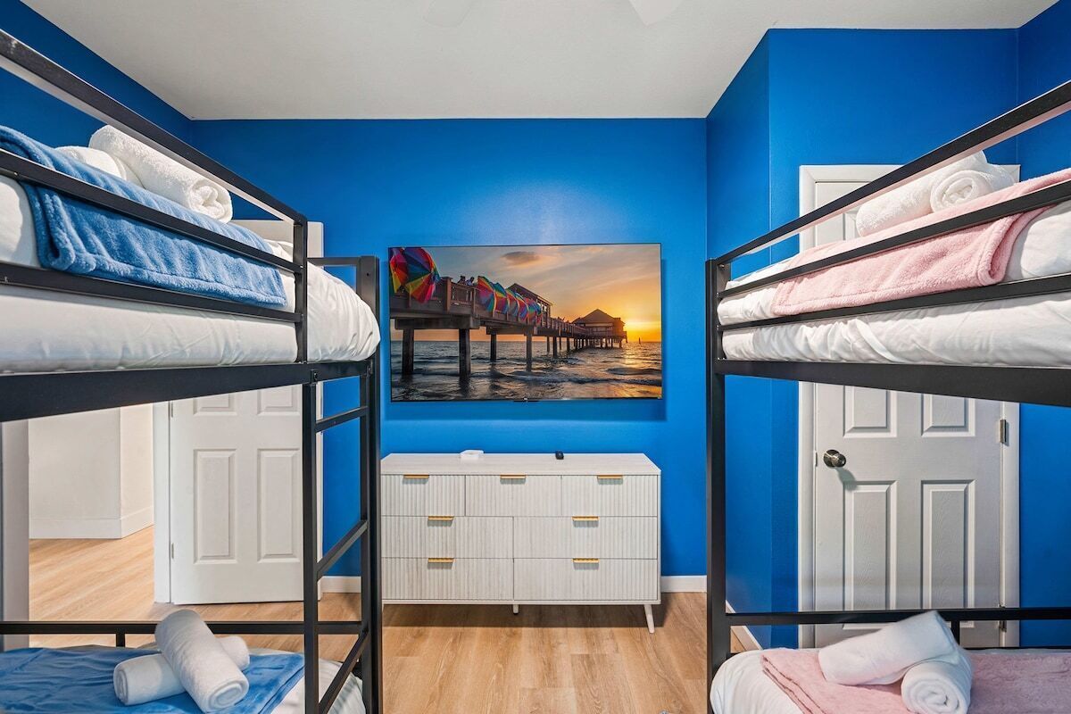 A room with bunk beds, a white dresser, and a painting of a pier at sunset.