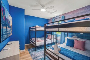 A room with bunk beds, a ceiling fan, a painting of a beach, and a desk with a remote control. - Entire home in Seminole, Florida, United States (Seminole)