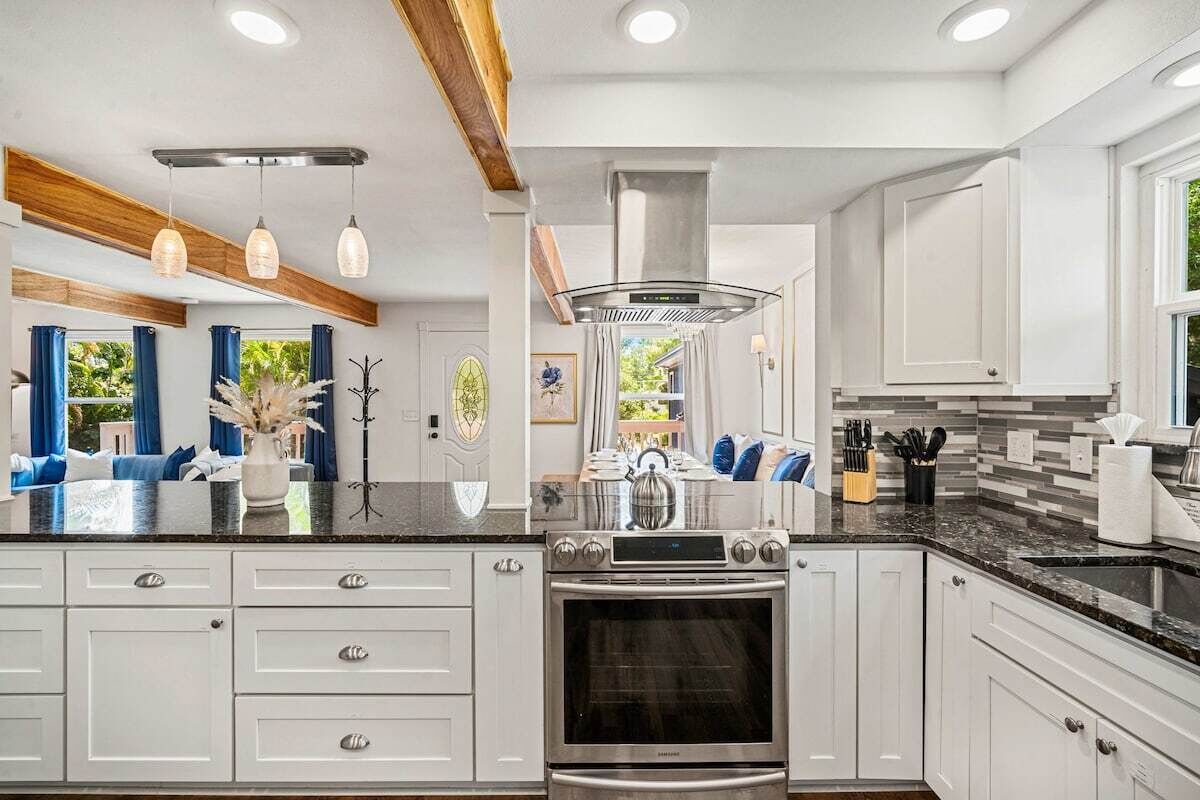 A modern kitchen with white cabinetry, a stainless steel range hood, and a central island with a kettle.