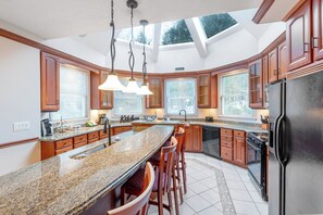 Cocina con una isla grande, encimeras de granito, armarios de madera, un refrigerador negro y un tragaluz.