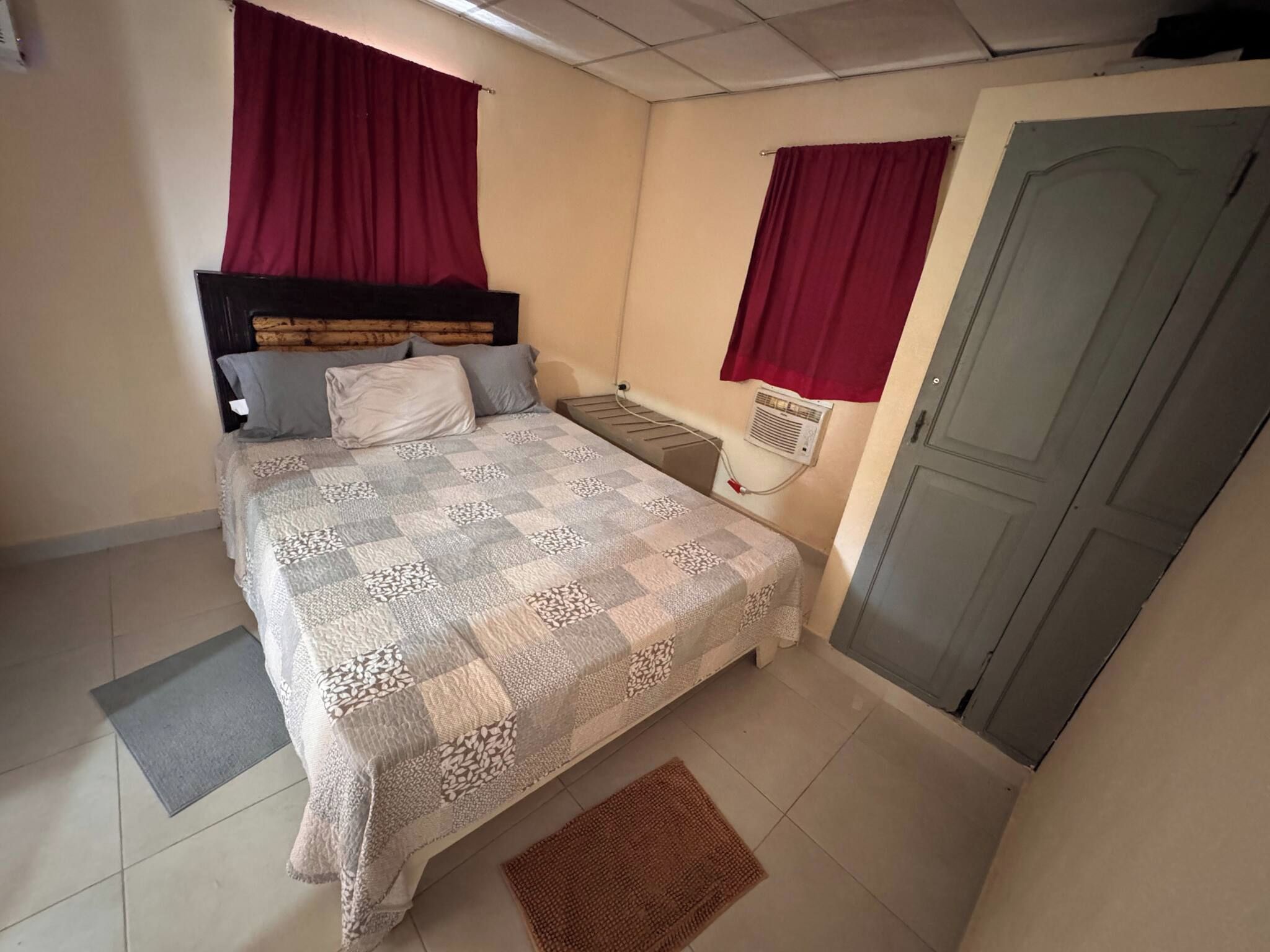 A bedroom with a bed, a radiator, a door, and a window with curtains.