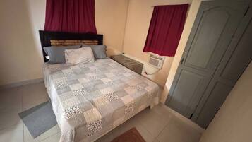 A bedroom with a bed, a radiator, a door, and a window with curtains.