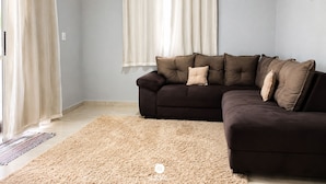 A living room with a dark brown sofa, beige rug, and light-colored curtains.