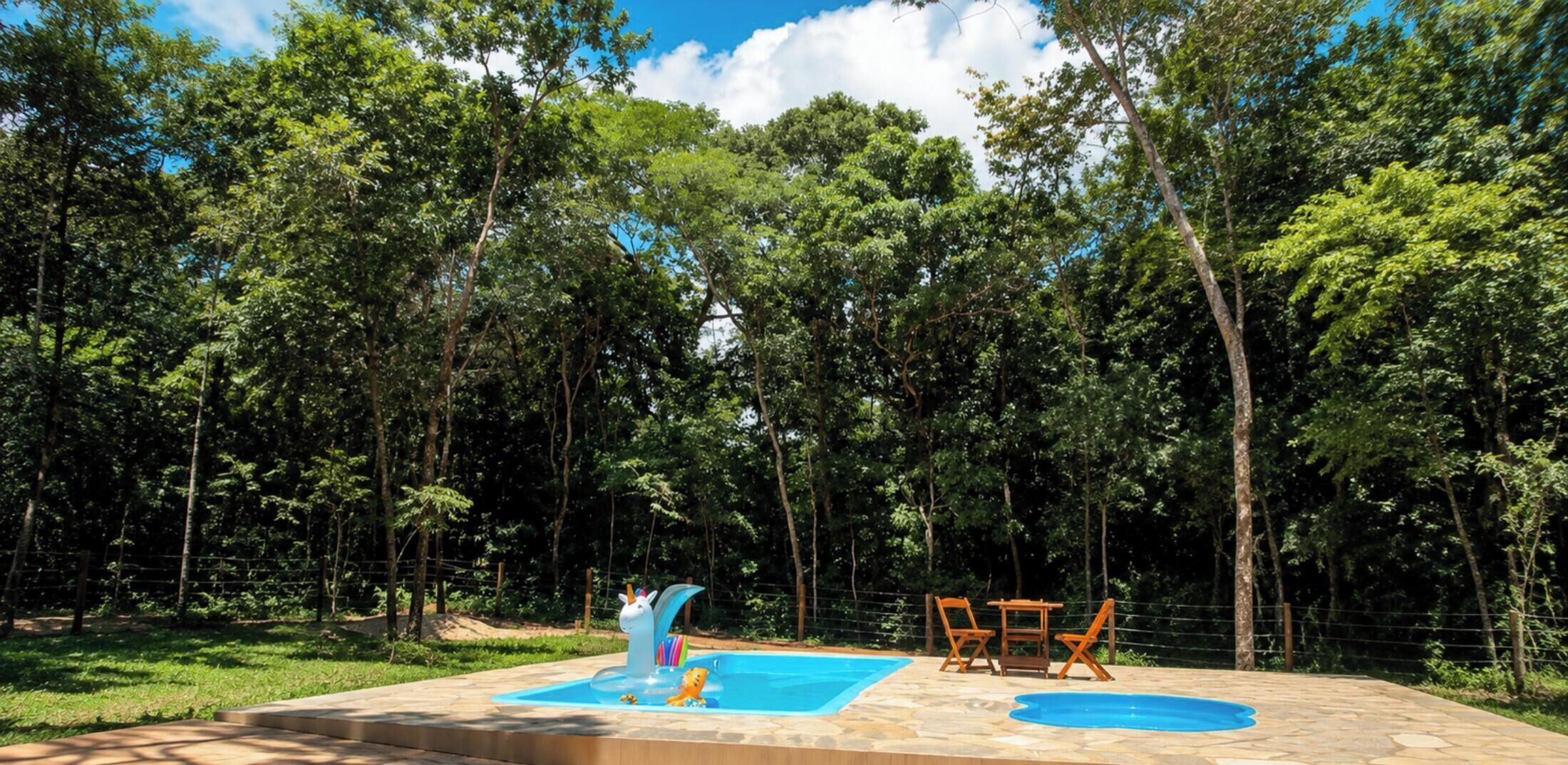 Una piscina con tobogán, rodeada de una valla y árboles.