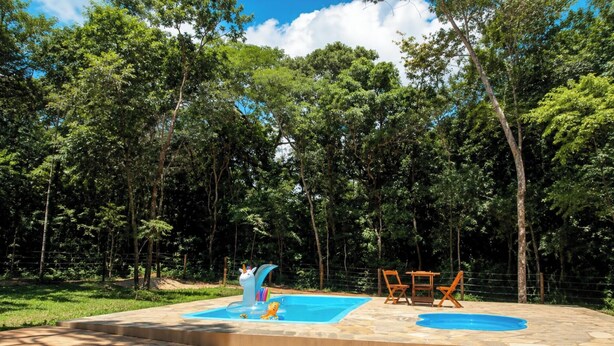 A swimming pool with a slide, surrounded by a fence and trees.